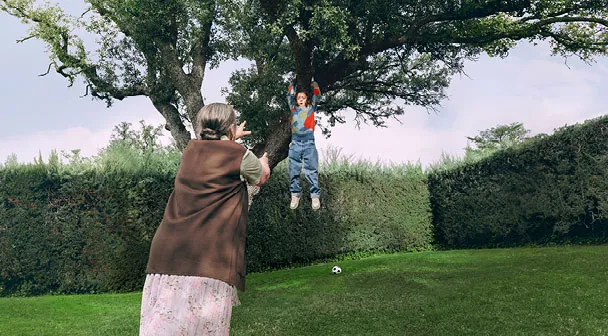 Ein Kind hängt mit den Armen an einem Baum und droht zu fallen, während eine ältere Dame zu dem Kind eilt um es zu fangen.